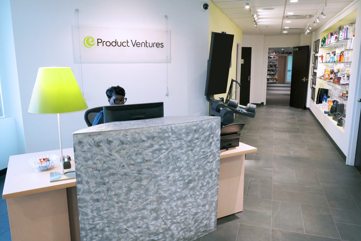 A woman sits at an office desk surrounded by shelves of medication